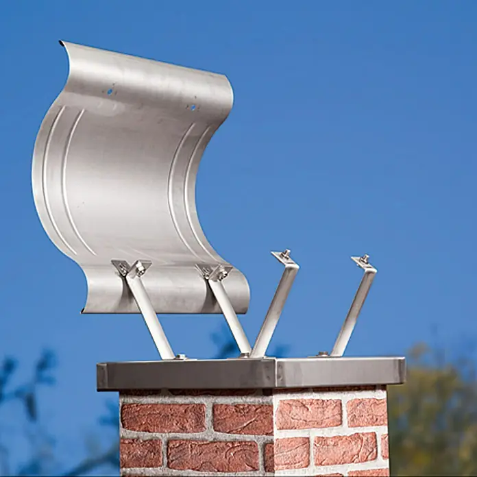 Sarei Kaminhauben-Umbauset - Edelstahl - Nahaufnahme einer Chimney Cricket Regenkappe aus Metall, die auf einem Ziegelkamin installiert ist, mit blauem Himmel im Hintergrund.