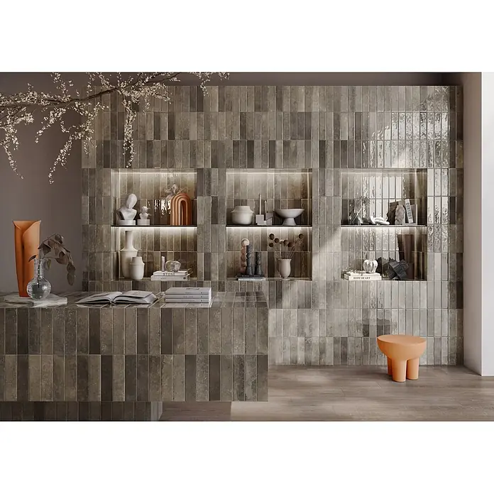 Wandfliese Portofino - 6,5 x 26 cm, Greige, Glänzend - Dunkle, rechteckige Fliesen schmücken vertikal eine Wand mit beleuchteten Regalen und einer passenden Theke in einem modernen Interieur.