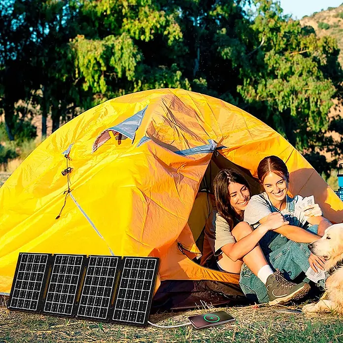 EDM Panel solar Plegable - Potencia nominal: 15 W, L x An x Al: 0,3 x 48,5 x 19,5 cm - Panel solar plegable negro cargando un smartphone al aire libre. Ubicado junto a una tienda de campaña amarilla con dos personas y un perro.