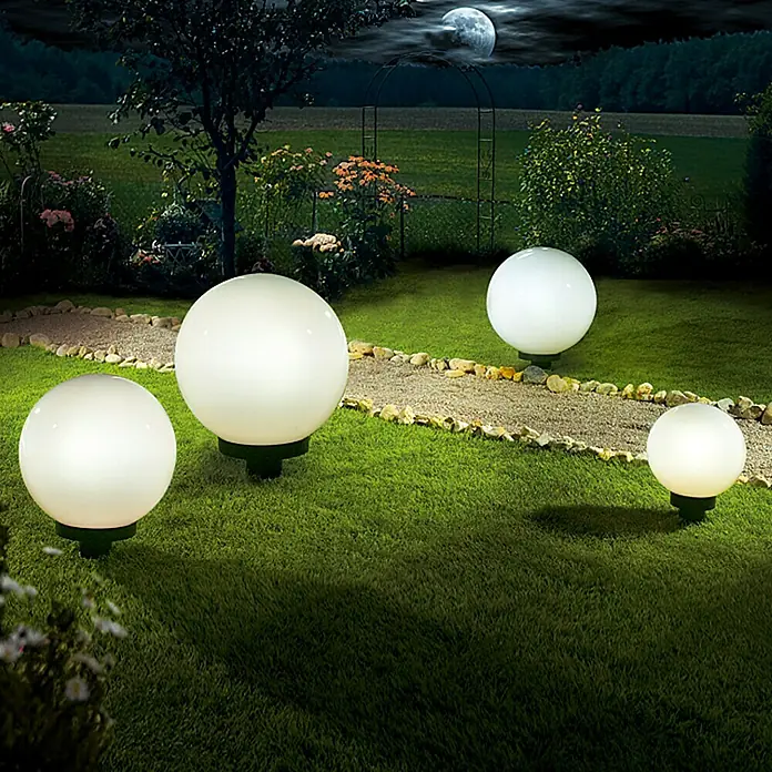 Starlux Kugel-Außenleuchte Kira20 cm, Weiß - Gartenansicht bei Nacht mit vier leuchtenden kugelförmigen Gartenleuchten, die entlang eines Kiesweges aufgestellt sind.