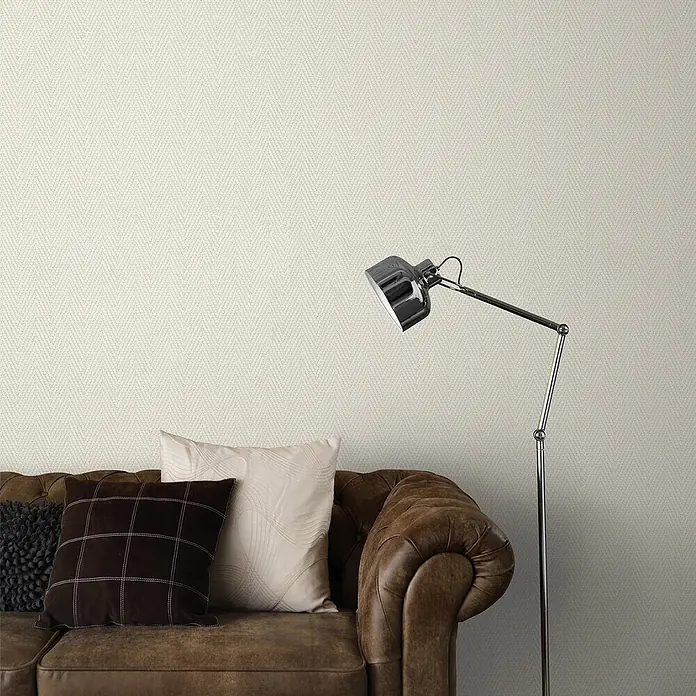 Erismann Papel pintado de vinilo Espiga - Beige, Gráfico, 10 x 0,53 m - Papel pintado crema con sutil textura de espiga, decorando una pared de salón detrás de un sofá de cuero marrón y una lámpara cromada.