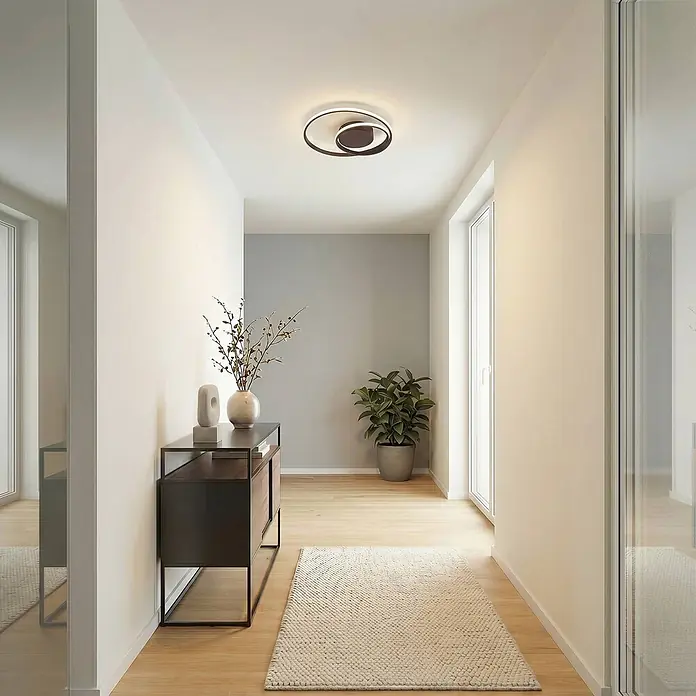 Lindby Deckenleuchte Emisua - schwarz - Moderne schwarz-weiße LED-Deckenleuchte mit abstraktem, verschlungenem Design, die einen Flur beleuchtet.