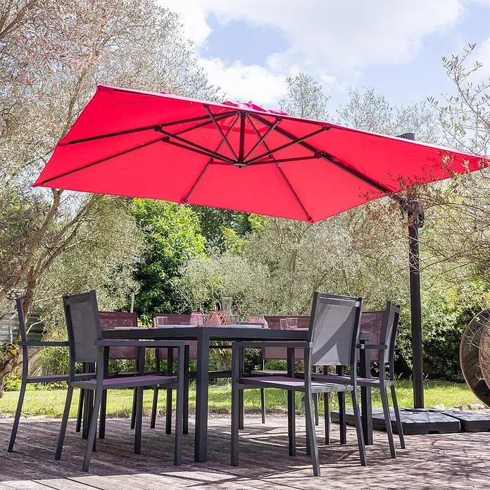 Freistehender Sonnenschirm MOLOKAI quadratisch 3x3m fuchsia + Hülle -  - Großer roter Ampelschirm beschattet eine dunkelgraue Outdoor-Essgruppe mit Stühlen auf einer Holzterrasse.