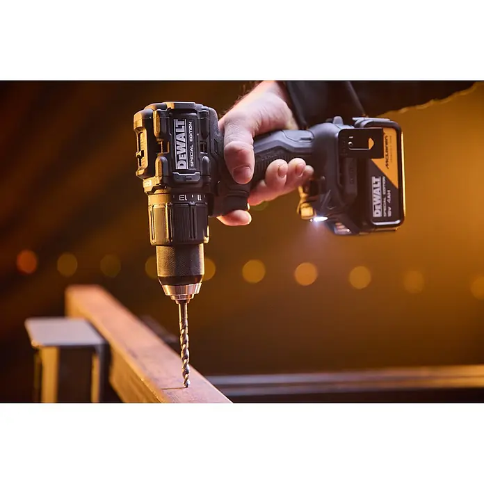 DeWalt Taladro percutor de batería McLaren DCD86MM2T - 18 V, 2 baterías, 4 Ah, 90 Nm - Una mano sostiene un taladro DEWALT edición especial negro y amarillo con batería McLaren, listo para perforar una viga metálica.