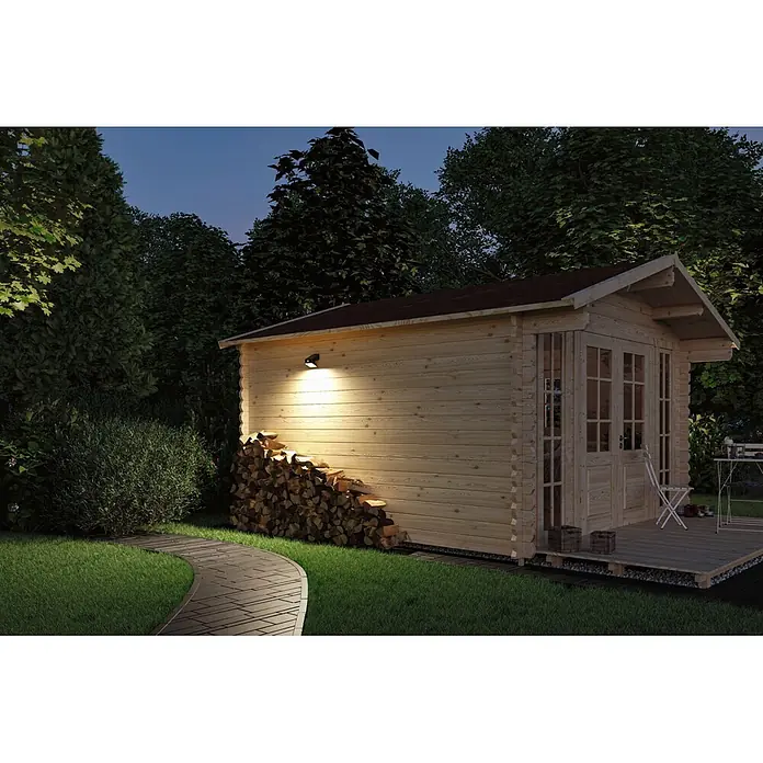 Paulmann Solarleuchte Lesly - Lichtfarbe: Warmweiß, LED, Höhe: 138 mm - Ein helles Holz-Gartenhaus in der Abenddämmerung, beleuchtet von einer Außenleuchte, mit einem Stapel Brennholz und einer kleinen Terrasse im grünen Garten.
