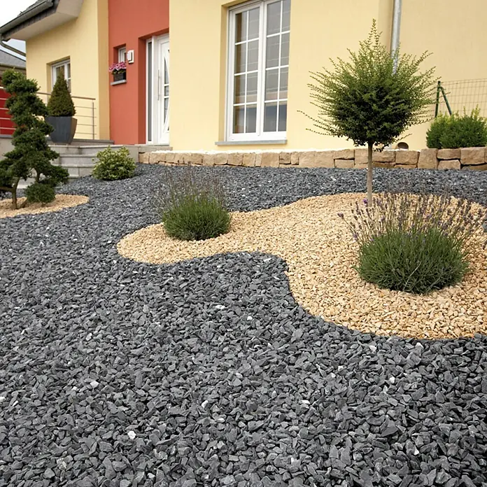 Gardol Premium Steinvlies - Polypropylen, 6 x 1 m - Das Bild zeigt einen Vorgarten mit verschiedenen Steinen, Pflanzen und einem kleinen Baum vor einem gelben Haus mit roter Tür.