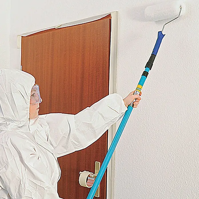 Wisent Arbeitsoverall - Damen, Weiß, L - Eine Person im Schutzanzug streicht eine Wand mit einer Farbwalze auf einem blauen Verlängerungsstab, um die Decke zu erreichen.