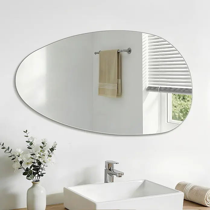S'AFIELINA Wandspiegel Forma Pure 850 × 500 mm - 85 x 50 cm - Kieselförmiger Silber-Spiegel über einem weißen Badezimmerwaschbecken, der Fenster und Handtuch reflektiert.