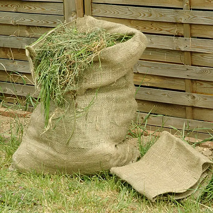 Floraworld Classic Gartensack - Natur, 105 cm - Sack aus Sackleinen gefüllt mit Grasschnitt vor einem Holzzaun.