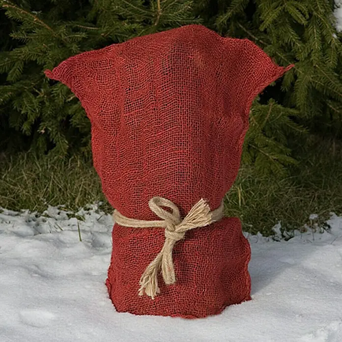 Floraworld Classic Gartensack - Rot, 80 cm - Eine rote Jutetuch-Pflanzenabdeckung mit einer Bindeschnur sitzt im Schnee vor immergrünen Bäumen und Sträuchern und schützt Topfpflanzen.