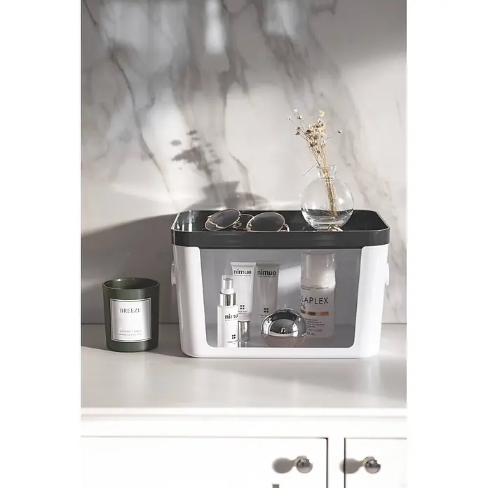 SmartStore Vorratsdose Compact Access - L x B x H: 20 x 29,5 x 16 cm, Kunststoff, Weiß - Ein weiß-schwarzer Aufbewahrungsbehälter mit Hautpflegeprodukten und Parfüm, neben einer grünen Kerze und Trockenblumen auf einer Theke.