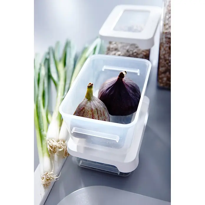 SmartStore Vorratsdose Snack - L x B x H: 12,5 x 9,5 x 4,5 cm, Kunststoff, Weiß - Zwei dunkle Feigen in einer transparenten Plastik-Frischhaltedose, gestapelt neben Frühlingszwiebeln auf einer Arbeitsplatte.