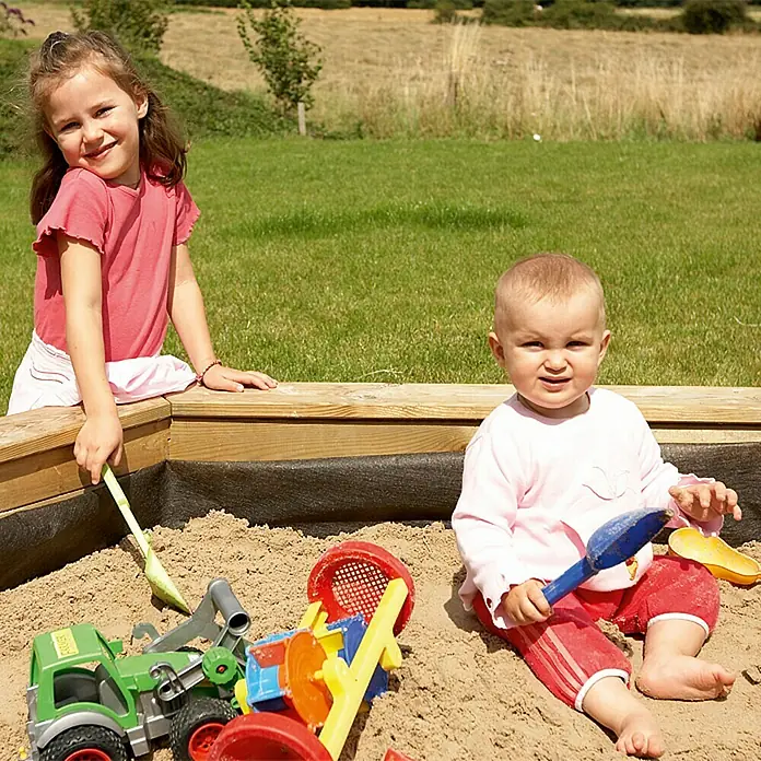 Gardol Sandkastenvlies - Polypropylen, L x B: 2 x 2 m - Zwei Kinder spielen in einem Sandkasten mit Sandspielzeug, darunter ein grüner Spielzeugtraktor und Schaufeln.