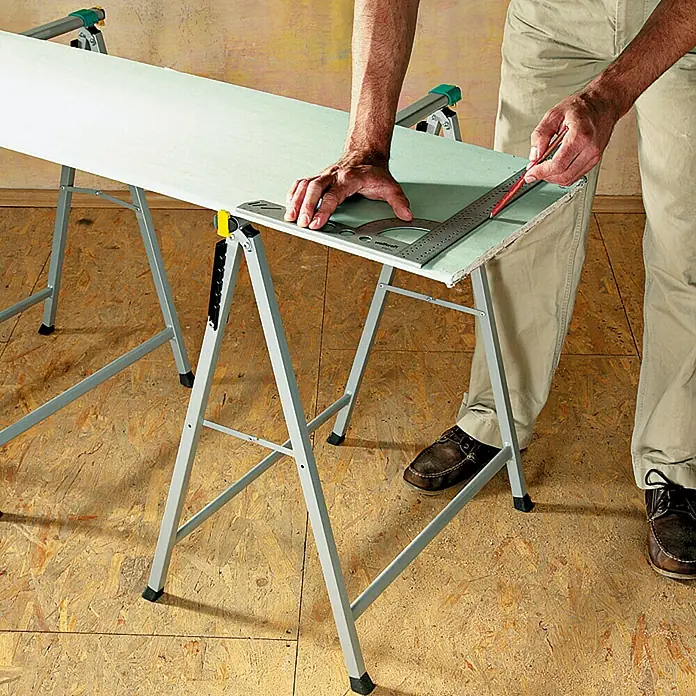 Auflagebock - Tragkraft: 100 kg - Trockenbauarbeiten: Ein Mann schneidet eine Gipskartonplatte mit Winkel und Bleistift auf zwei Arbeitstischen.