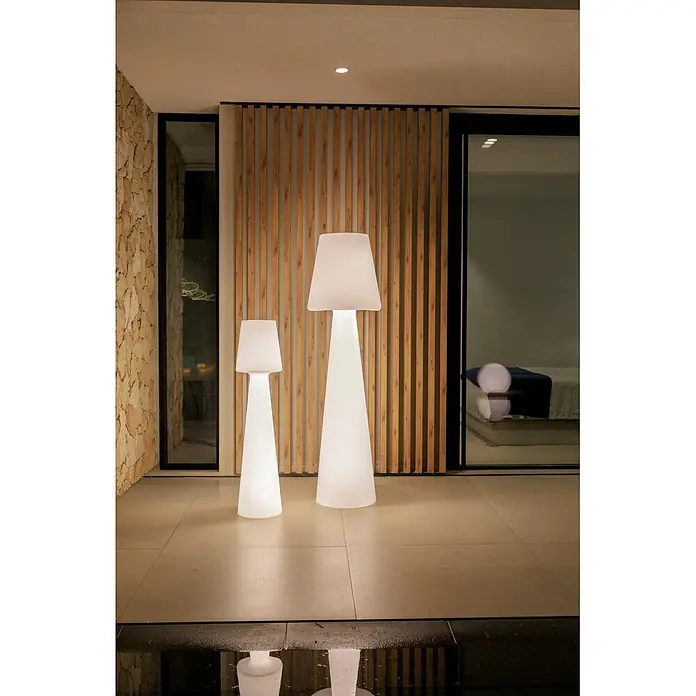 New Garden Lámpara de pie con batería Lola 165 Blanco - Blanco, Altura: 165 cm, RGB - Dos lámparas de pie cónicas blancas iluminadas, una más grande y una más pequeña, en un patio y reflejadas en el agua.