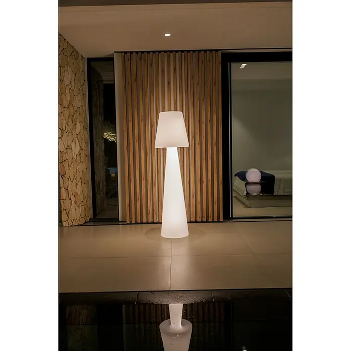 New Garden Lámpara de pie con batería Lola 165 Blanco - Blanco, Altura: 165 cm, RGB - Lámpara de pie moderna blanca iluminada con base cónica y pantalla rectangular, reflejándose en el agua en un ambiente contemporáneo.