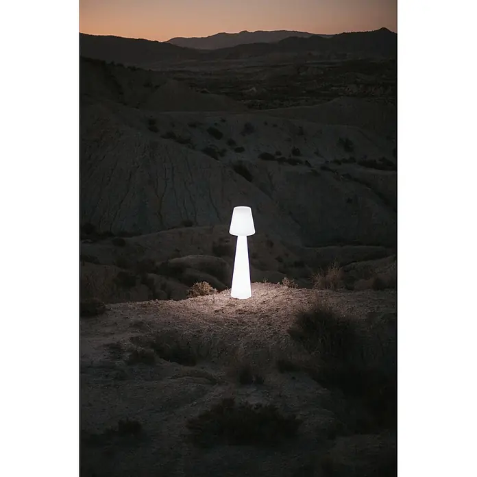 New Garden Lámpara de pie con batería Lola 165 Blanco - Blanco, Altura: 165 cm, RGB - Lámpara blanca alta y brillante iluminando un paisaje montañoso oscuro y árido al anochecer.