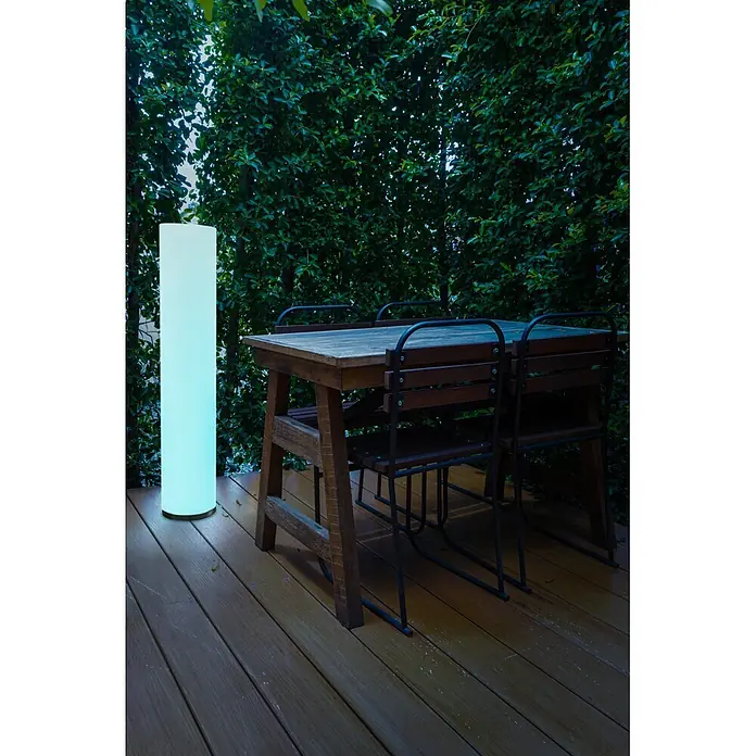 New Garden Lámpara de diseño para exterior Fity 100 - 9,5 W, Blanco, Ø x Al: 19 x 100 cm, RGB - Lámpara de pie cilíndrica alta para exteriores con un gradiente de luz azul-verde, iluminando una terraza y mesa de madera.