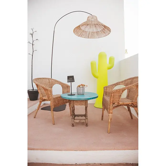 New Garden Lámpara de pie con batería Niza 230 - Marrón, 155 x 80 x 230 cm, Blanco cálido - Salón exterior con dos sillas de mimbre, una mesa turquesa y una gran lámpara de pie de mimbre, complementado con una escultura de cactus amarillo.