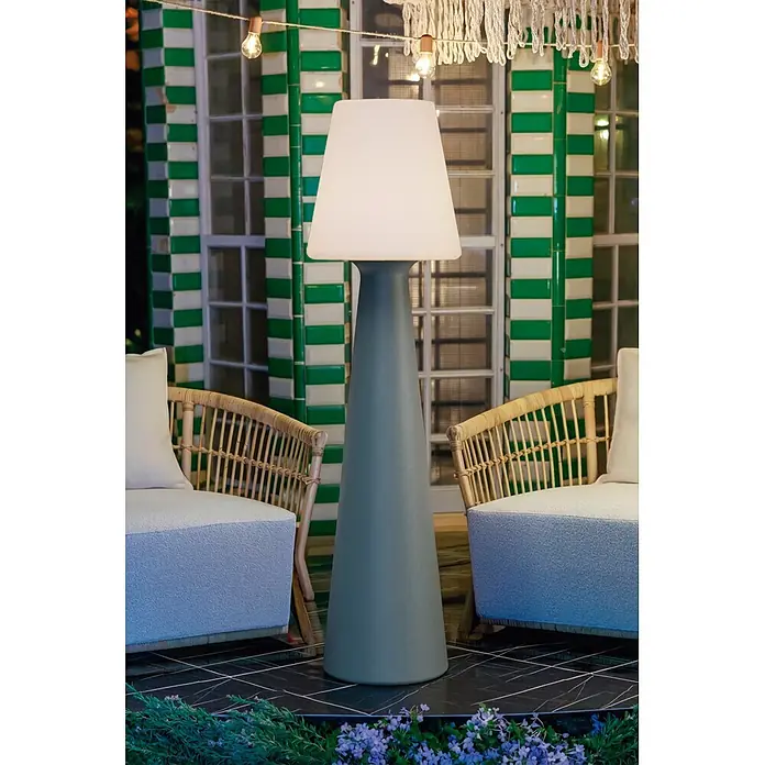 New Garden Lámpara de pie con batería Lola 165 Cemento - Cemento, Altura: 165 cm, Blanco neutro - Lámpara de pie alta para exterior con base cónica gris y pantalla blanca, situada entre dos sillas de ratán.