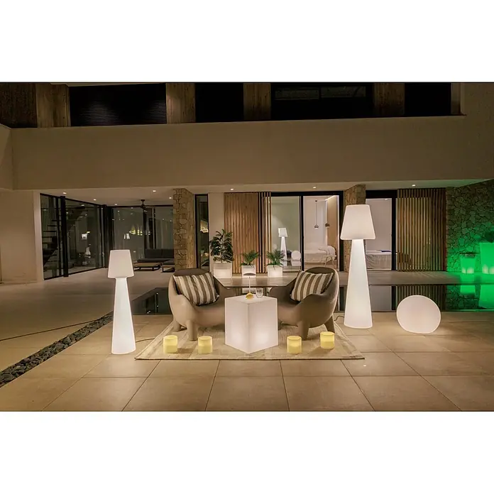 New Garden Lámpara de pie con batería Lola 110 - Blanco, Altura: 110 cm, RGBW - Zona de salón exterior iluminada de noche con muebles blancos luminosos: sillones, mesa auxiliar, lámparas y maceteros.