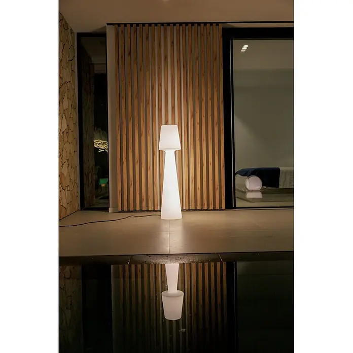 New Garden Lámpara de pie con batería Lola 110 - Blanco, Altura: 110 cm, RGBW - Lámpara de pie blanca brillante en un patio, reflejada en agua oscura, iluminando la escena nocturna.