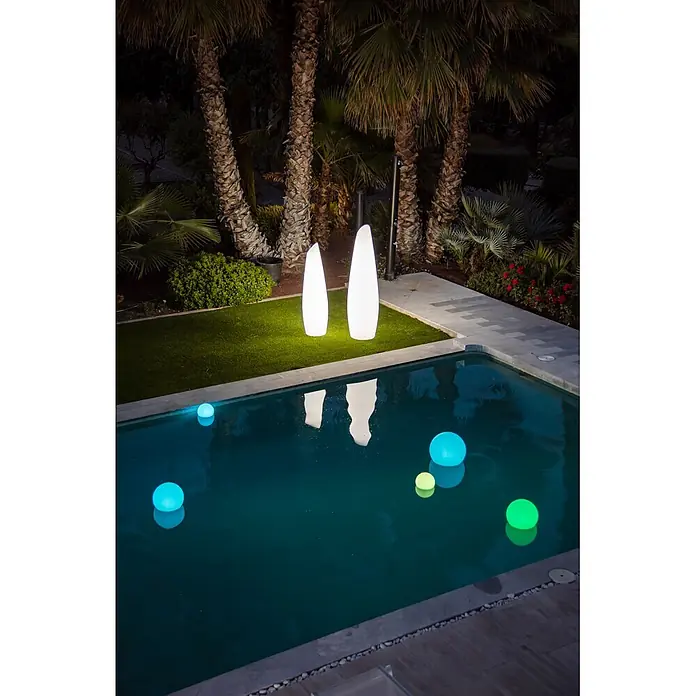 New Garden Lámpara de pie con batería Fredo 140 - 1,3 W, Blanco, Ø x Al: 38 x 139 cm, RGB - Dos luces de jardín blancas e iluminadas sobre césped artificial y varias esferas flotantes de colores e iluminadas en una piscina de noche.