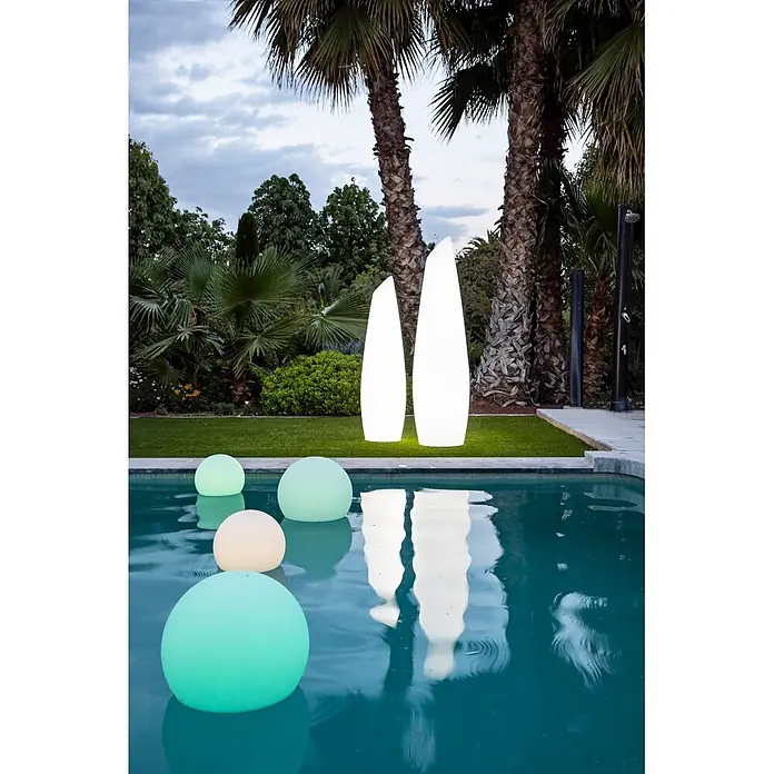 New Garden Lámpara de pie con batería Fredo 140 - 1,3 W, Blanco, Ø x Al: 38 x 139 cm, RGB - Esferas luminosas pastel flotan en una piscina, junto a dos altas luces de pilar blancas y brillantes en el césped.