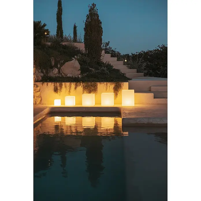 New Garden Lámpara solar Cuby 40 LED - 1 W, Blanco, Color de luz: RGBW, L x An x Al: 40 x 40 x 40 cm - Cinco luces de cubo blancas luminosas de varios tamaños iluminan el borde de una piscina por la noche, reflejándose en el agua.