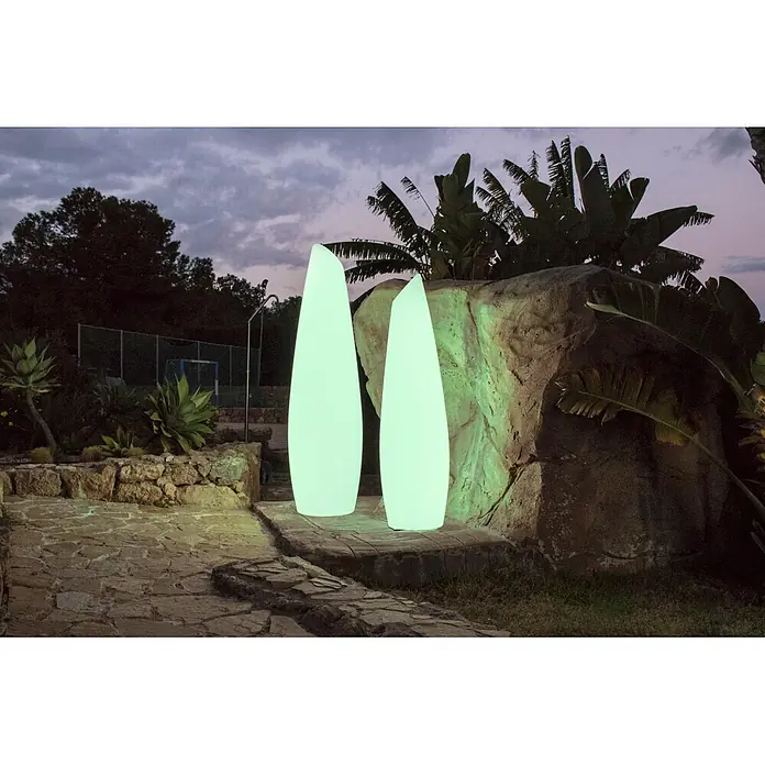 New Garden Lámpara de pie para exterior Fredo 140 - 18 W, Blanco, Ø x Al: 38 x 139 cm, Blanco cálido - Dos lámparas exteriores altas, iluminadas de verde claro, en un un camino de piedra al anochecer, emitiendo un suave resplandor.