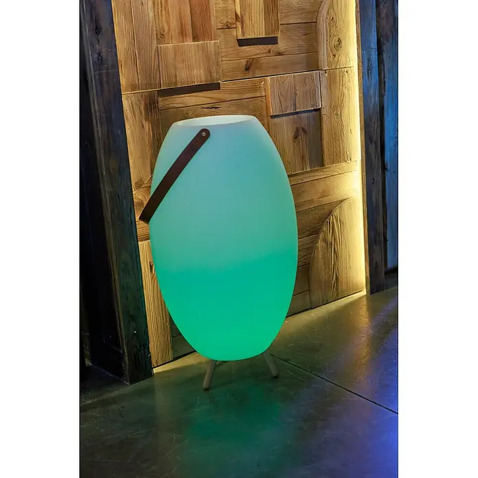 New Garden Lámpara para exterior con altavoz Apolo 70 - 6 W, Blanco, Ø x Al: 40 x 72,5 cm, RGBW, Altavoz - Lámpara portátil ovalada de color verde brillante con asa marrón y patas de madera, sobre pared de madera.