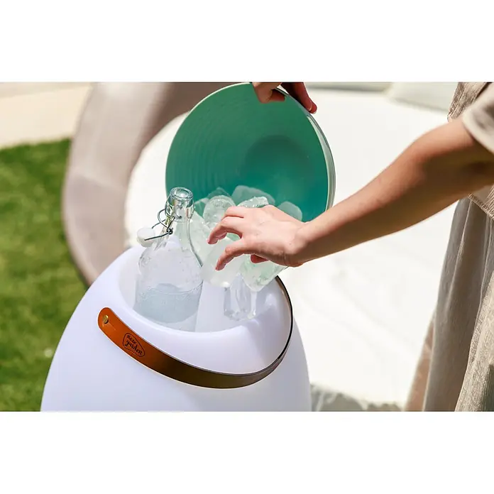 New Garden Lámpara para exterior con altavoz Apolo 70 - 6 W, Blanco, Ø x Al: 40 x 72,5 cm, RGBW, Altavoz - Una persona añade hielo a una nevera blanca luminosa con asa de cuero marrón, enfriando una botella al aire libre.