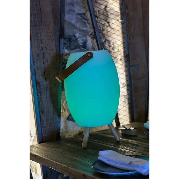 New Garden Lámpara para exterior con altavoz Apolo 45 - 6 W, Blanco, Ø x Al: 24 x 40,5 cm, RGBW, Altavoz - Lámpara portátil ovalada verde claro con asa de cuero marrón y patas de madera, sobre una mesa de madera.