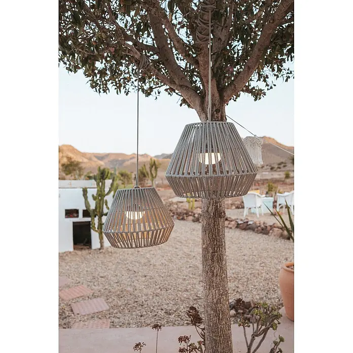 New Garden Lámpara colgante de batería Conta 30 - 9 W, Topo, Ø x Al: 40 x 30 cm, Blanco cálido - Dos lámparas colgantes grises trenzadas cuelgan de un árbol en un entorno exterior, con luz cálida.