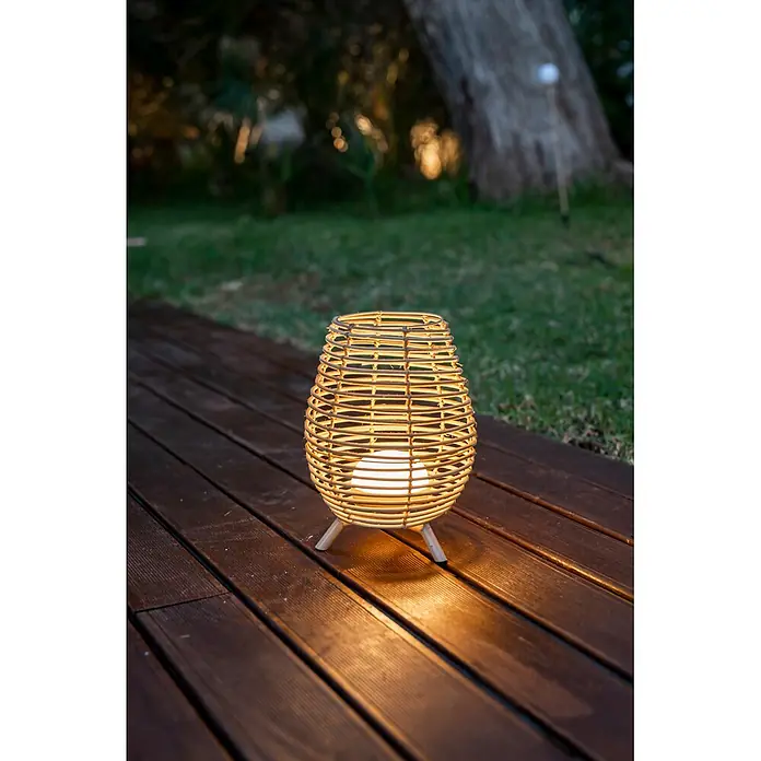 New Garden Bossa Lámpara para exterior a batería 30 - 9 W, Marrón, Blanco cálido, Ø x Al: 22,5 x 32,5 cm - Linterna de exterior de ratán natural con luz brillante, sobre una cubierta de madera oscura.