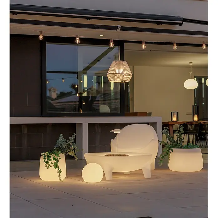 New Garden Conta Lámpara colgante de batería 30 - 9 W, Blanco, Ø x Al: 40 x 30 cm, Blanco cálido - Patio exterior al anochecer con muebles blancos iluminados, maceteros con vegetación y guirnaldas de luces cálidas, creando un ambiente acogedor.