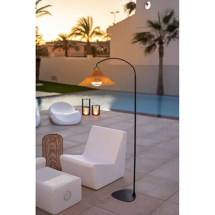 New Garden Lámpara de pie con batería Niza 165 - Marrón, 73 x 40 x 167 cm, Blanco cálido - Lámpara de pie de exterior con base arqueada negra y pantalla de fibras naturales tejidas, iluminando una zona de piscina.