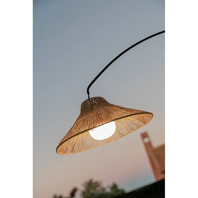 New Garden Lámpara de pie con batería Niza 165 - Marrón, 73 x 40 x 167 cm, Blanco cálido - Lámpara exterior colgante con pantalla de paja tejida natural, proyectando una luz cálida contra el cielo vespertino.
