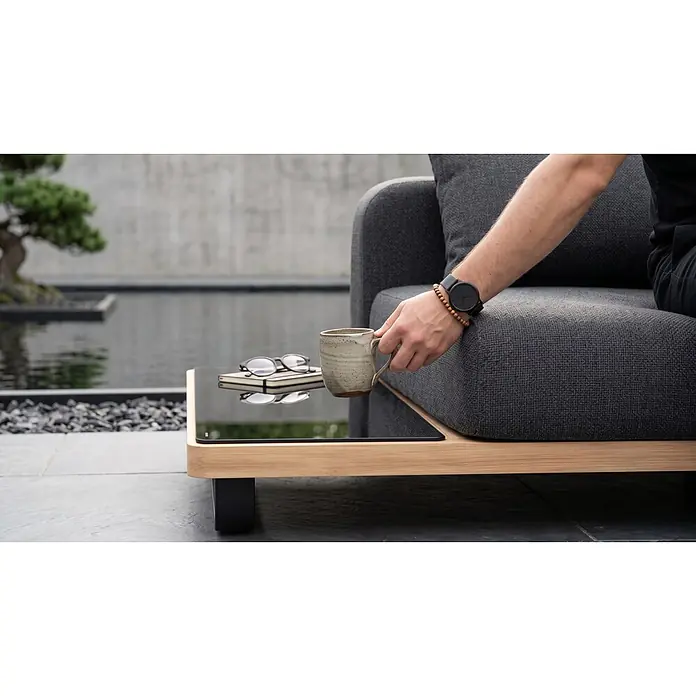 Sunfun Conjunto de muebles Cintia - 6 pzs., Aluminio/Poliéster, Antracita - Sofá de exterior gris oscuro con mesa auxiliar integrada de madera clara y cristal negro, con taza y gafas.