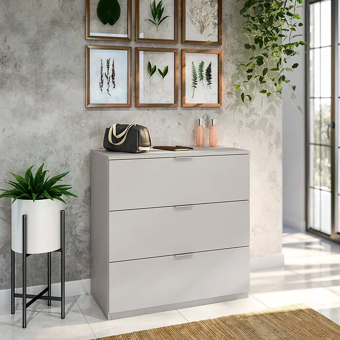 Set muebles de dormitorio Cachemir - 3 pzs., Beige Cachemir, Vestidor con montaje reversible - Cómoda gris claro de 3 cajones en una habitación moderna, con elegantes tiradores plateados y un diseño minimalista, con objetos decorativos.