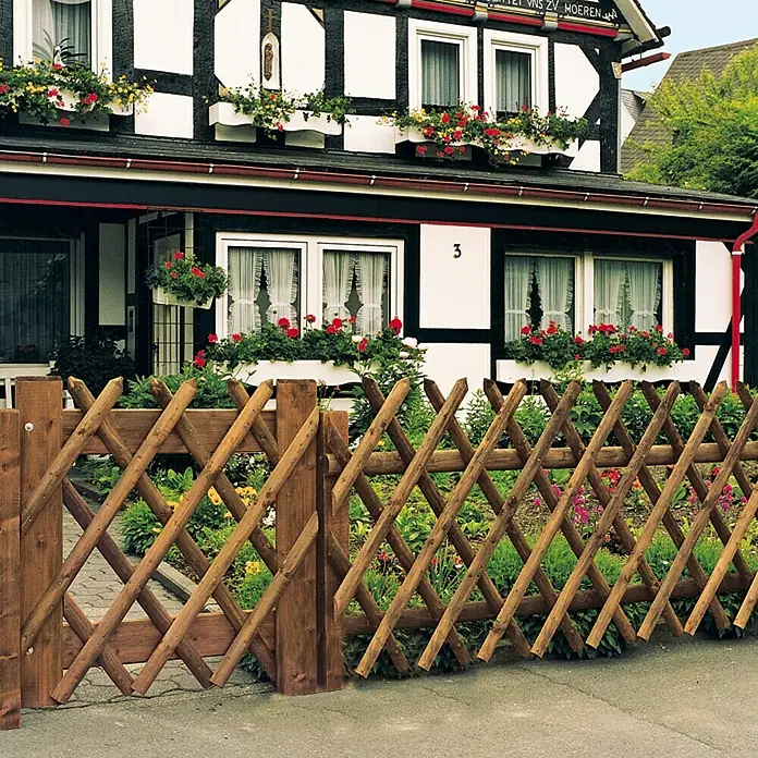 Joda Jägerzaun - 250 x 80 cm - Eine rustikale, braune Jägerzaun-Einfriedung vor einem traditionellen Fachwerkhaus, die Garten und Gebäude harmonisch verbindet.