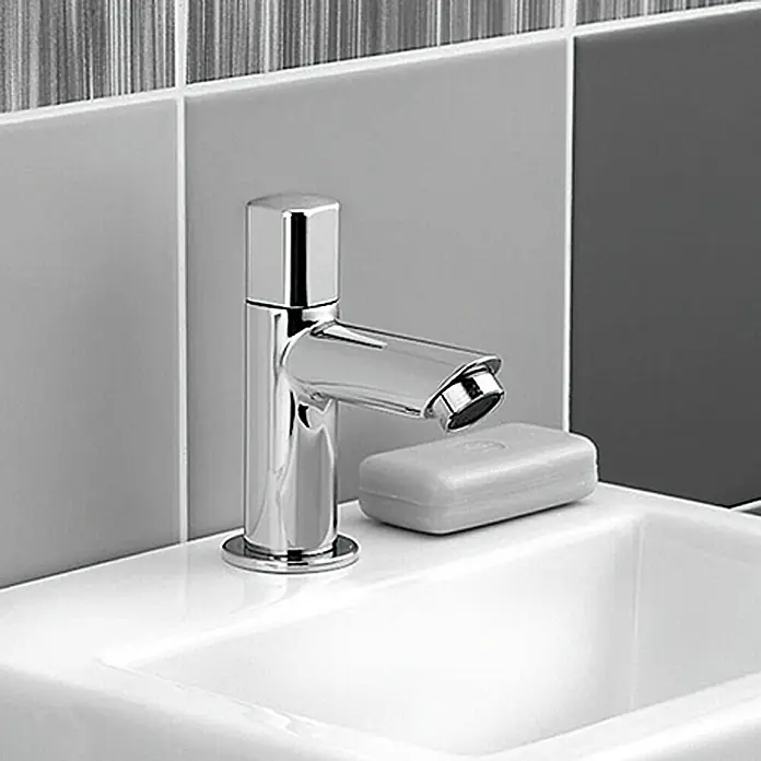 Camargue Kaltwasser-Standventil Bali/Milan - Chrom, Glänzend - Nahaufnahme einer modernen Armatur mit glänzendem Chromfinish und einem Stück Seife auf einem weißen Waschbecken, vor einem Hintergrund aus grauen Fliesen.