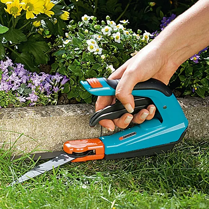 Gardena Comfort Grasschere - Antihaftbeschichtet, Ergonomisch - Eine Hand bedient eine Gardena Akku-Grasschere ComfortCut zum Trimmen von Rasenkanten vor einem Blumenbeet.