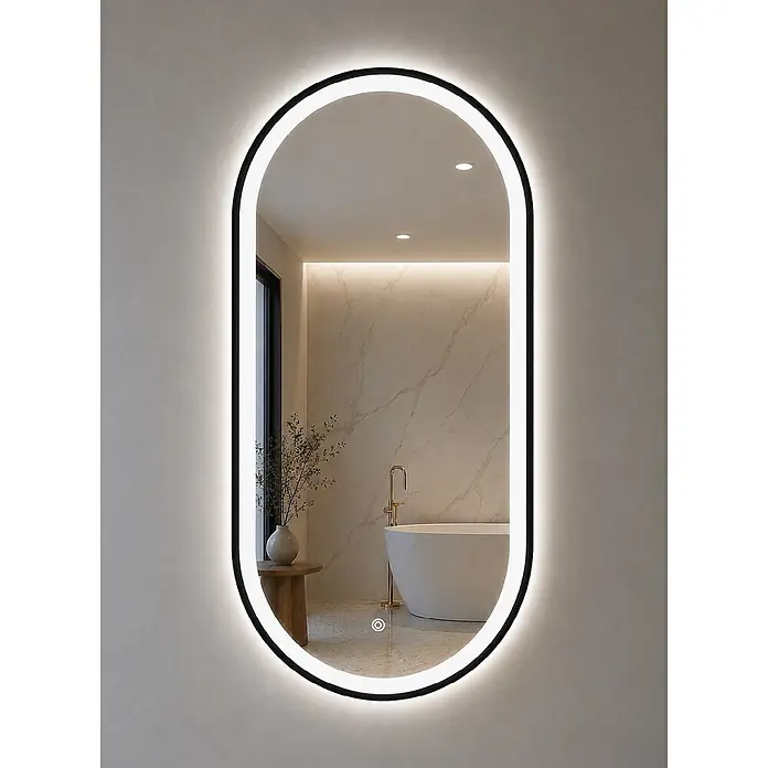Cordia Lichtspiegel - 50 x 100 cm, Schwarz - Ovaler LED-Spiegel mit schwarzem Rahmen und beleuchtetem Lichtstreifen, der ein modernes Badezimmer mit freistehender Badewanne und Pflanze reflektiert.
