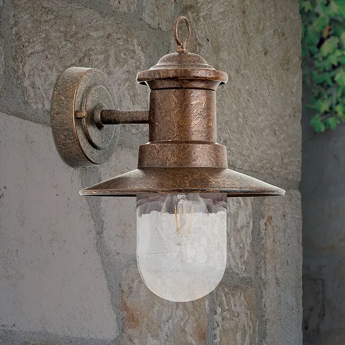 Orion Leuchten Außenwandleuchte Leonie - 60 W, Braun, Klar, IP44 - Wandleuchte aus gealterter Bronze mit Klarglas und sichtbarer Glühlampe, an Steinmauer montiert.