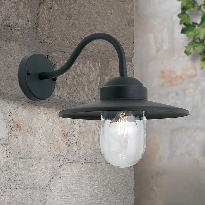 Orion Leuchten Außenwandleuchte Edward - 60 W, Schwarz, Klar, IP44 - Dunkelgraue Metall-Außenwandleuchte mit klarem Glasschirm und sichtbarer Glühlampe, an einer strukturierten Steinwand montiert.
