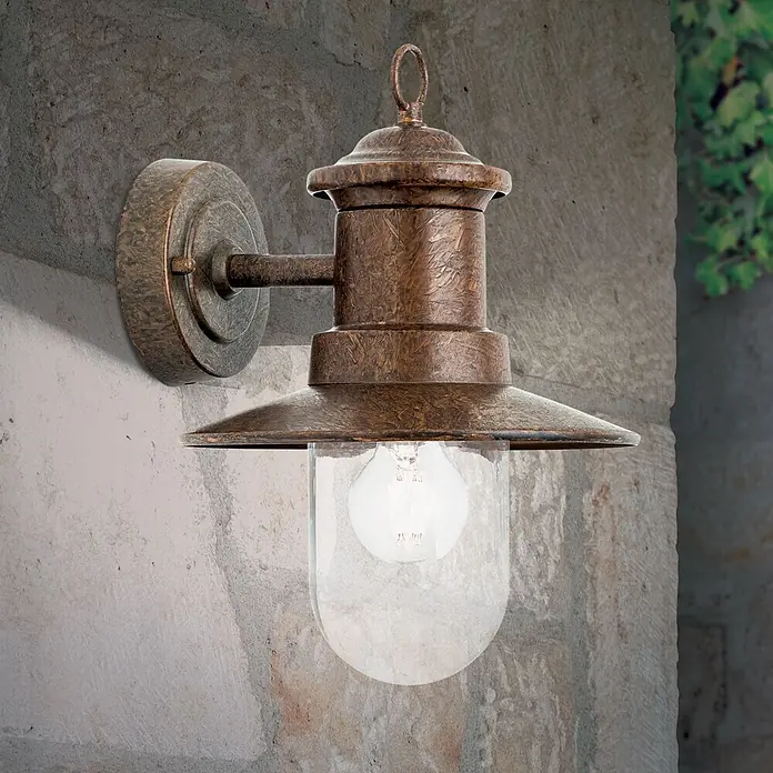 Orion Leuchten Außenwandleuchte Leonie - 60 W, Braun, Klar, IP44 - Rustikale Außenwandleuchte aus Antikbronze mit klarer Glasscheibe und sichtbarer Glühbirne, an Steinmauer montiert.