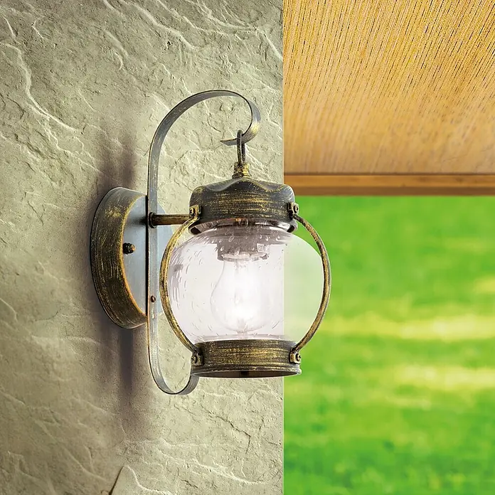 Orion Leuchten Außenwandleuchte Taverna - 60 W, Schwarz, Klar, IP23 - Wandleuchte aus gealtertem Bronze-Gold mit klarem, blasigem Glas, an einer strukturierten Steinwand montiert.