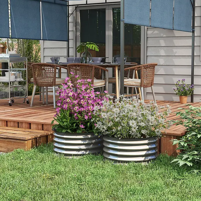 SONNENH Hochbeet modulares 2er-Set, rund - Metall, silber - Zwei geriffelte Hochbeete aus Metall, gefüllt mit leuchtend rosa und weißen Blumen, stehen auf dem Rasen neben einer Holzterrasse.