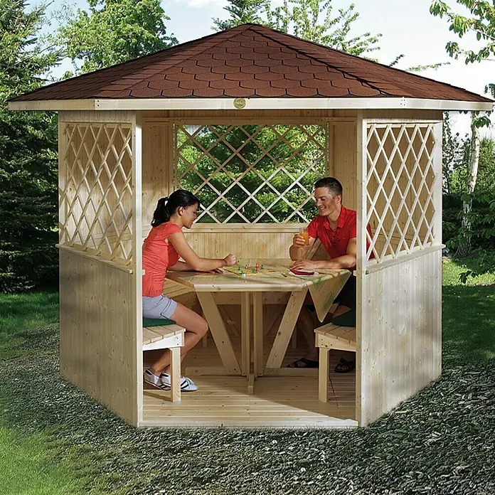 Weka Gartenlaube Königsee - 4,29 m², Fichte - Eine hölzerne Gartenlaube mit einem braunen Dach, in der zwei Personen an einem Tisch sitzen und ein Spiel spielen.